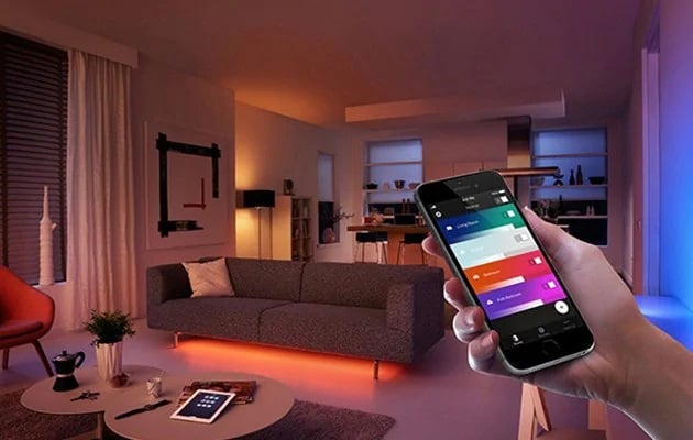 Hånd bruger smartphone til at fjernbetjene farverig smart belysning