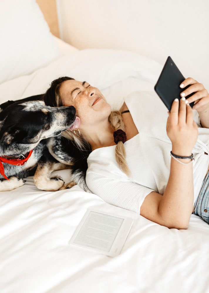 Kvinde ligger på en seng med en Kobo e-bogslæser og en hund ved siden af