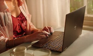Kvinde der skriver på HP computer mens hun drikker kaffe
