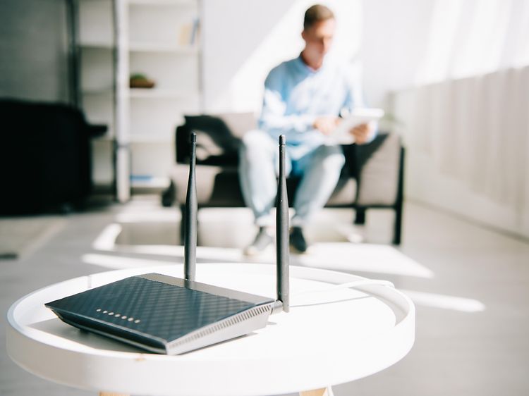 Trådløs router på et bord mens en mand sidder i baggrunden og kigger på sin tablet