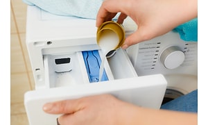 Hånd der hælder vaskemiddel i vaskemaskinen