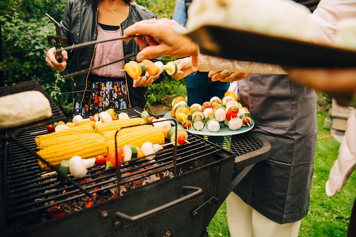 Folk, der står omkring en kulgrill og griller grøntsager