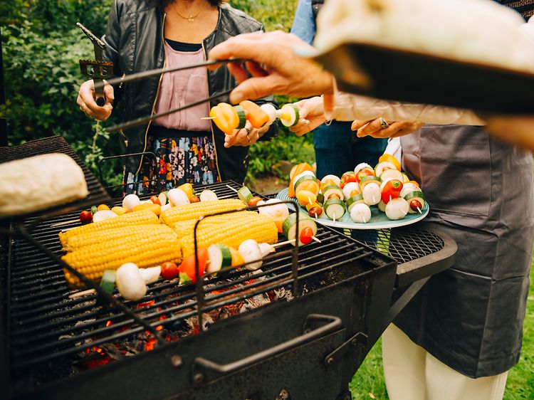 Folk, der står omkring en kulgrill og griller grøntsager