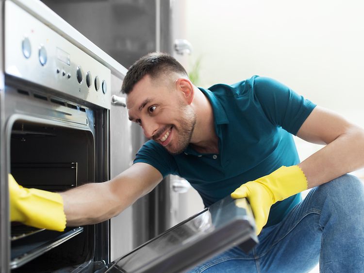Mand renser ovn med gule handsker