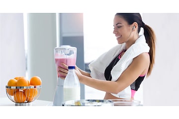 kvinde i sportstøj laver pink smoothie med en blender