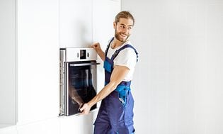 Mand i blå kedeldragt fjerner en indbygget ovn i et hvidt køkken