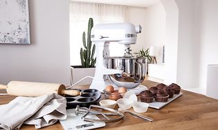 Køkkenmaskine på et bord med bageudstyr, muffins og æg