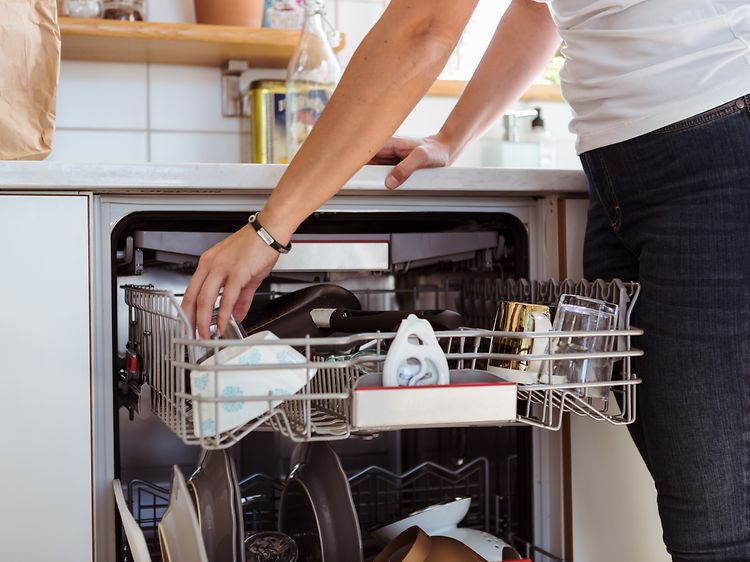 En kvinde læner sig over en køkkenbænk med en åben opvaskemaskine