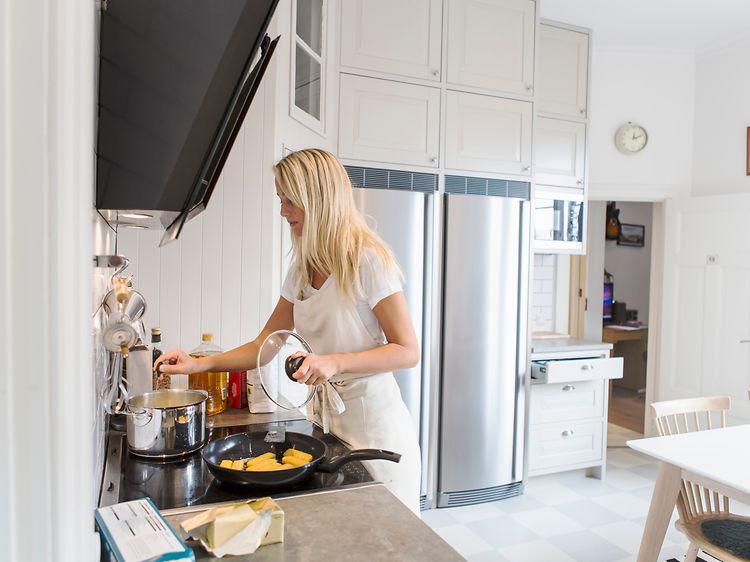 Kvinde laver mad i køkken med et køleskab og et fryseskab i baggrunden