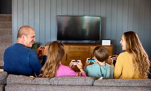 En familie på 4 sidder i en sofa og spiller Nintendo Switch sammen