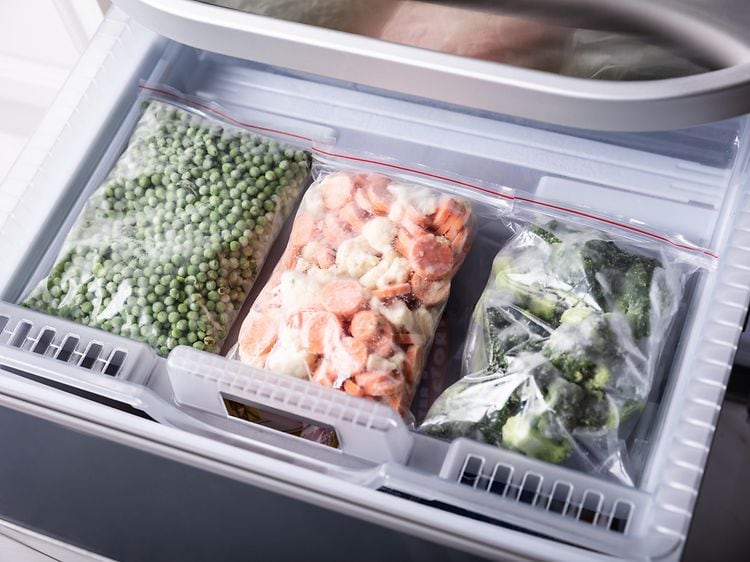 Tre plastikposer med frosne grøntsager i en fryser