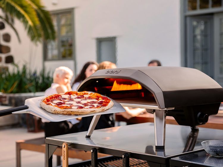 En pizza foran en pizzaovn med mennesker i baggrunden