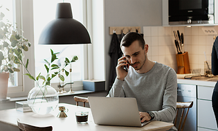 En mand, der arbejder på sin bærbare computer og taler på sin smartphone i et køkken