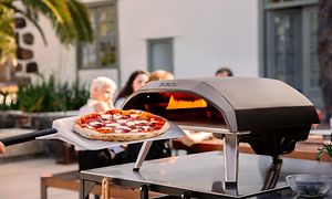En pizza foran en ovn med folk i baggrunden 