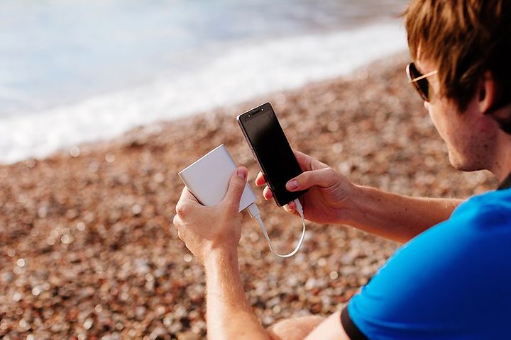 Mand på strand oplader sin smartphone med en powerbank