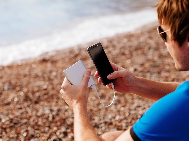 Mand på strand oplader sin smartphone med en powerbank