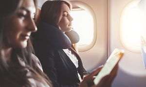 To kvinder slapper af i et fly, den ene med en nakkepude og den anden kigger på sin telefon