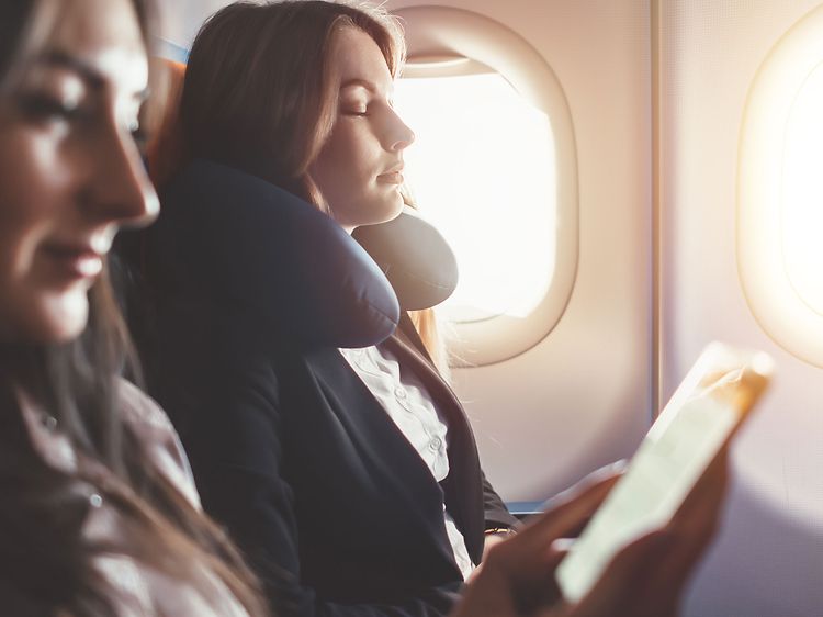 To kvinder slapper af i et fly, den ene med en nakkepude og den anden kigger på sin telefon