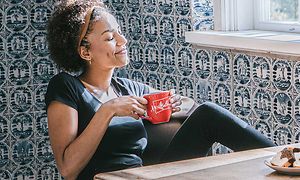 Kvinde drikker af en kaffekop ved bord med kaffemaskine på