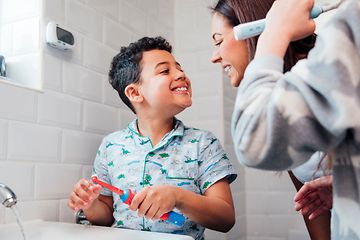 Familie på badeværelset og en lille dreng, der viser sine tænder til sin mor og holder en elektrisk tandbørste i hånden