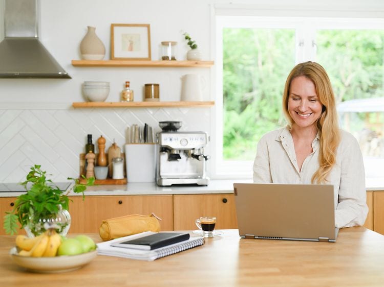 En kvinde sidder i sit køkken og arbejder på sin laptop