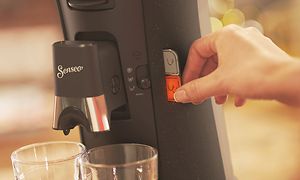 Hånd trykker på en knap på Senseo Select kapselkaffemaskine