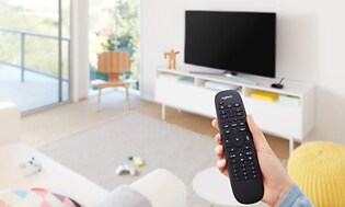 Hånd der betjener Logitech-fjernbetjening foran TV og medieafspillere, i stuen