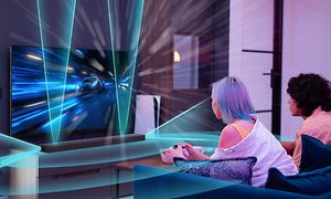 Billede af to personer der spiller på et TV over Sony HT-A7000 soundbar der udsender lyd i alle retninger, illustreret i blåt