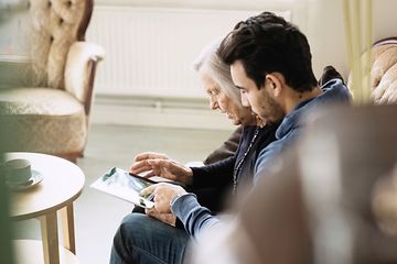 Billede af en ældre mand og en yngre mand i gang med at kigge på en tablet