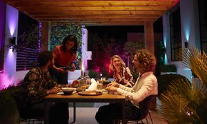 Mennesker der spiser udenfor ved et spisebord omgivet af forskelligfarvet smart belysning
