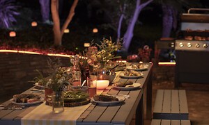 Udendørs spisebord på terrasse med have i baggrunden med monteret smart belysning
