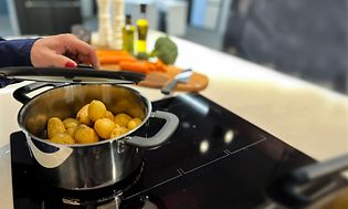 En hånd der sætter låget på en gryde med kartofler