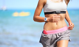 Telecom - sportswatch - kvinde der løber på stranden iført et sportswatch og pulsbælte