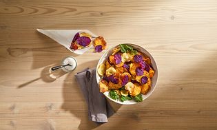 Fried vegetable chips and salt on table seen from above