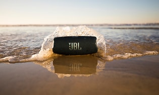 JBL Charge 5 på strandkanten med en bølge over sig