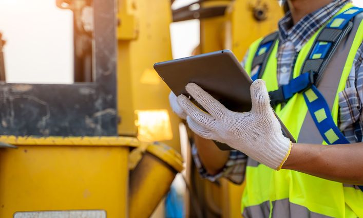 Bygningsarbejder, der bruger tablet udendørs på en byggeplads, med handsker på