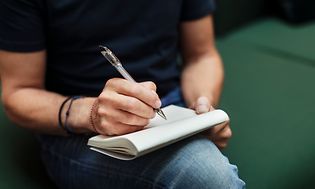 Mand skriver med en kuglepen på et stykke papir