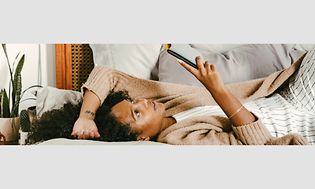 Kvinde ligger på en sofa med en telefon i hånden