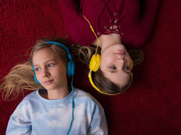 To piger med hovedtelefoner ligger på et gulv