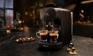 En sort L'OR Barista kapselmaskine og to kopper nybryggede espresso og to espresso kaffekapsler
