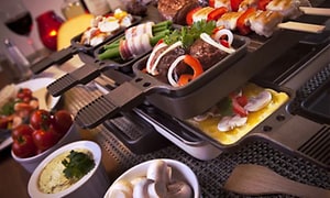 Nærbillede af en firkantet raclette fuld af mad, der tilberedes