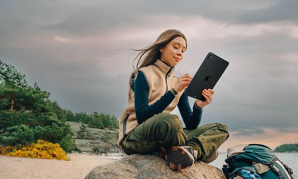 iPad i hånden på en kvide, som sidder på en strand