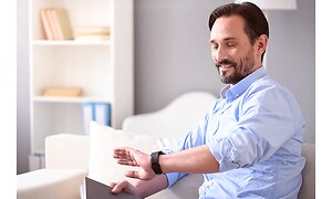 Mand der smiler og kigger på sit smartwatch