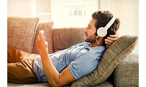 Mand der slapper af på en sofa med headset og telefon